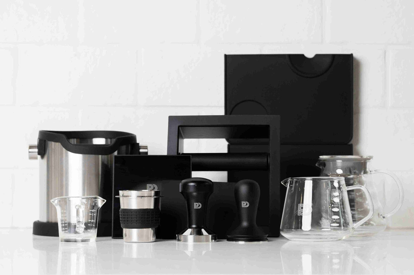 Philip & Douglas knock boxes, tampers, dosing cup, shot glass and glass coffee servers on a counter