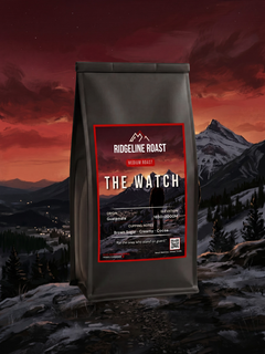 The Watch medium roast coffee bag, front view, against a deep red sunset over mountains