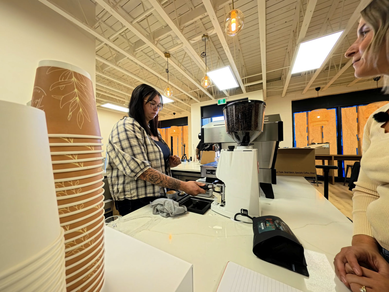 A barista at the Nest Cafe counter beside the grinder and a stack of cups